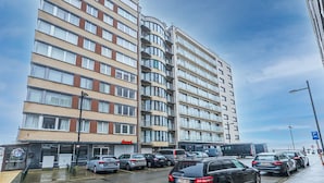 A multi-story hotel with a modern design, featuring a mix of brick and glass facades, and a parking area with several cars. - Apartment With 2 Bedrooms and sea View (Middelkerke)