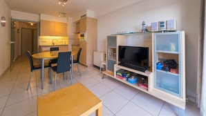 A modern living room with a TV, a glass cabinet, and a dining area with chairs and a table. - Apartment With 2 Bedrooms and sea View (Middelkerke)