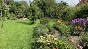 Um jardim bem cuidado com diversas plantas e flores, gramado e um caminho.