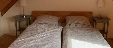 Una stanza con soffitto a falde, pavimento in legno e un letto con biancheria a righe. Sono presenti due comodini con lampade.