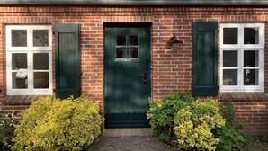 Um edifício de tijolos com porta verde, janelas emolduradas em branco e telhado ladrilhado.
