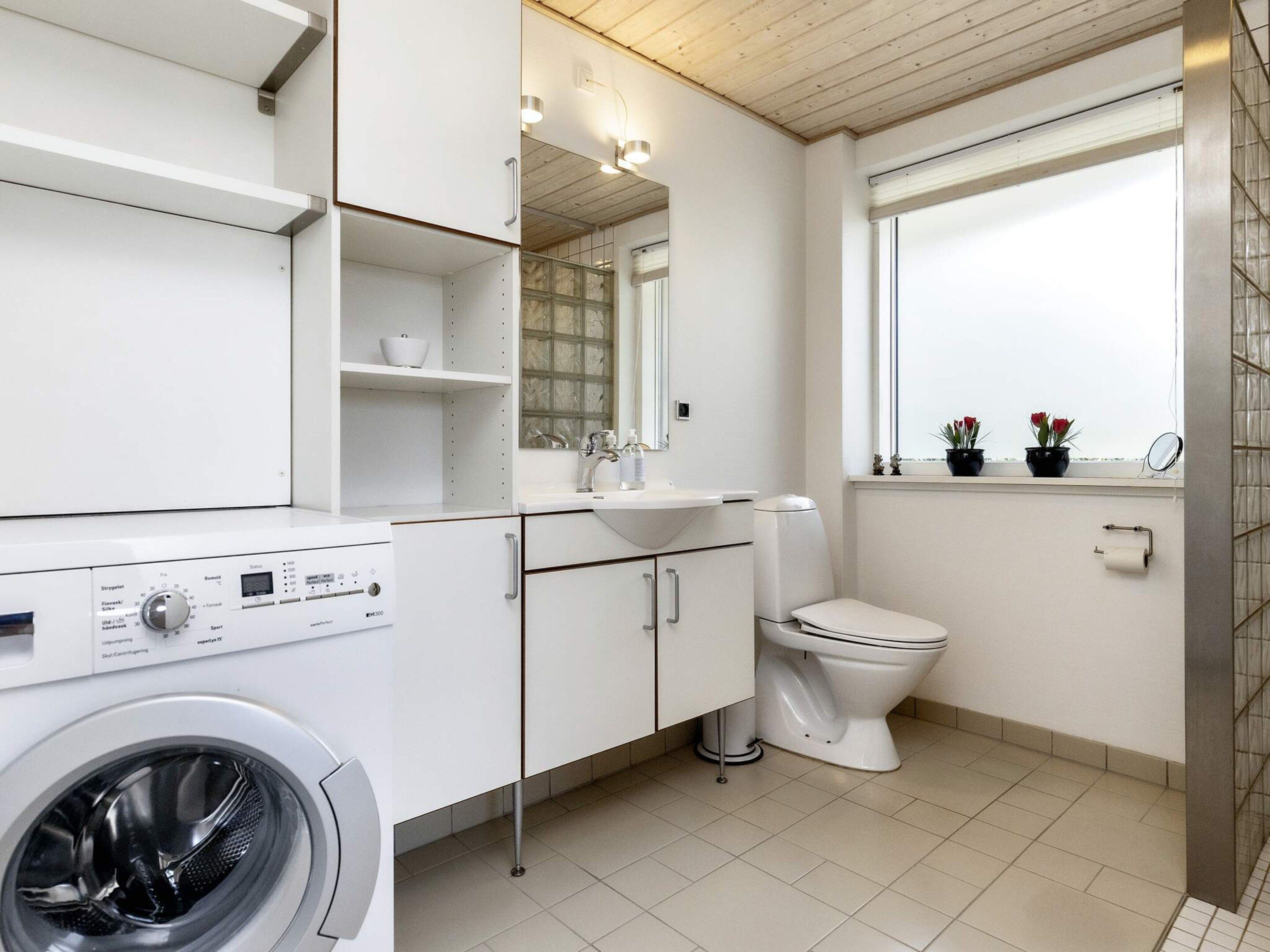 Et moderne badeværelse med vaskemaskine, toilet og et vindue med plantekasser.