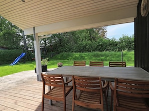 A covered outdoor patio with a table and chairs, a slide, and a garden view. - 4 Star Holiday Home in Hadsund (Hadsund)