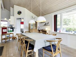 Un comedor con una mesa larga, sillas de madera, lámparas colgantes y vistas al exterior a través de un ventanal.