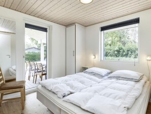 Un dormitorio con cama, una silla, un ventanal y una puerta que da a un espacio exterior.