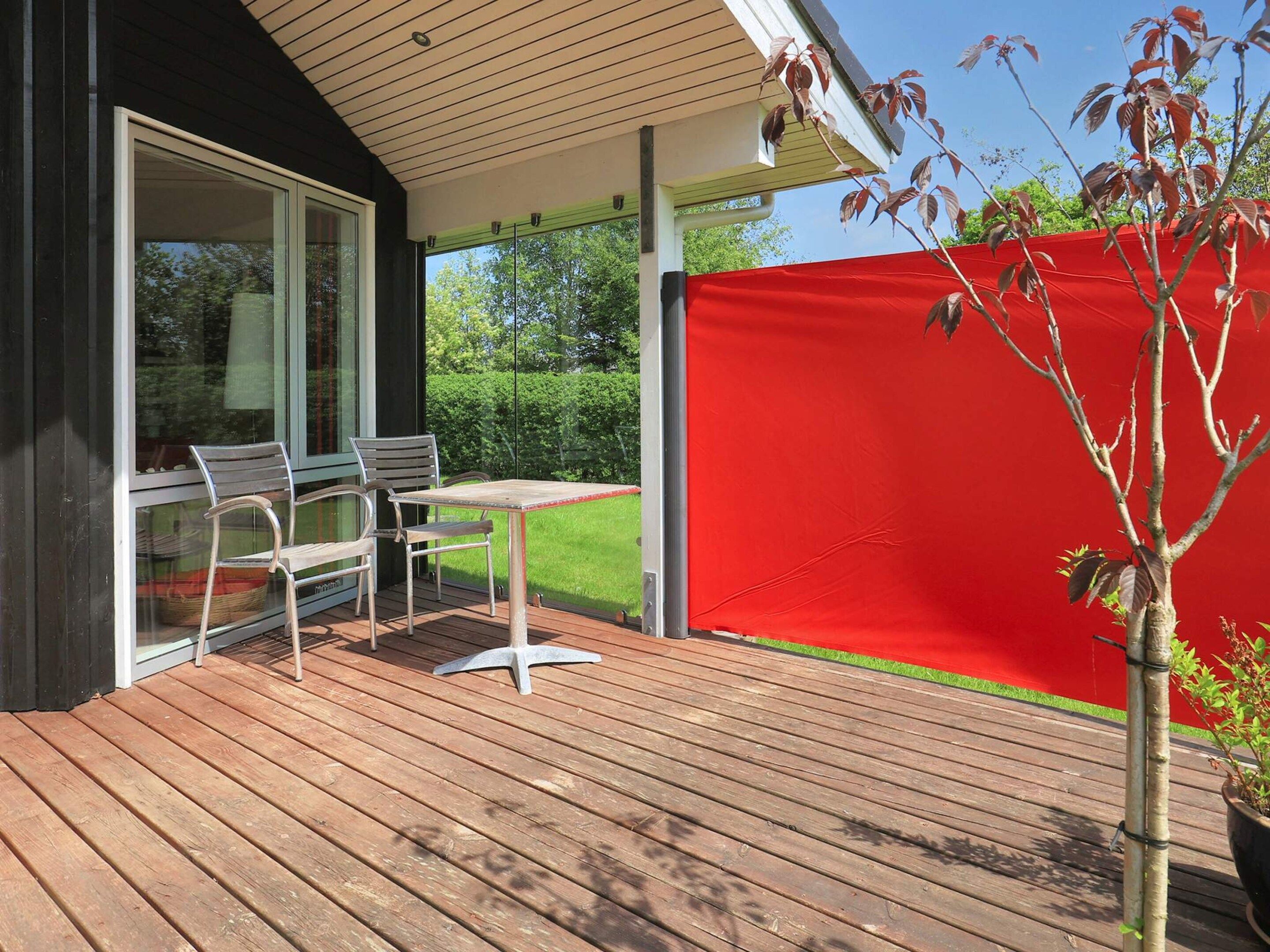 Un patio exterior con una mesa y sillas, un separador rojo para privacidad y una planta en maceta.