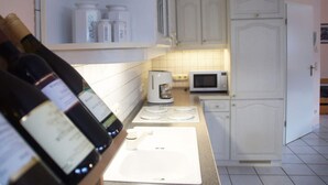A kitchen with white cabinets, a microwave, a coffee maker, and bottles on a shelf. - Holiday Apartment Pia Stadfeld (Mehring)