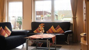 A living room with a black sofa, a small table, and a view of the outside through large windows. - Holiday Apartment Pia Stadfeld (Mehring)