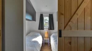 A narrow room with two beds, a small table with a lamp, and a window with curtains. - Cozy Chalet With Unobstructed Views (Hoogersmilde)