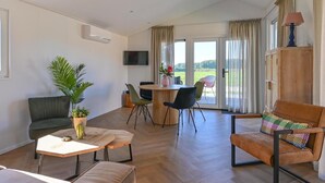 A spacious living area with a wooden floor, a sofa, a dining table with chairs, and a TV mounted on the wall. - Cozy Chalet With Unobstructed Views (Hoogersmilde)