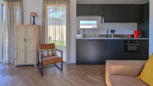 A modern kitchen with dark cabinets, a window, and a built-in oven. There is a wooden chair and a sofa with a yellow pillow. - Cozy Chalet With Unobstructed Views (Hoogersmilde)
