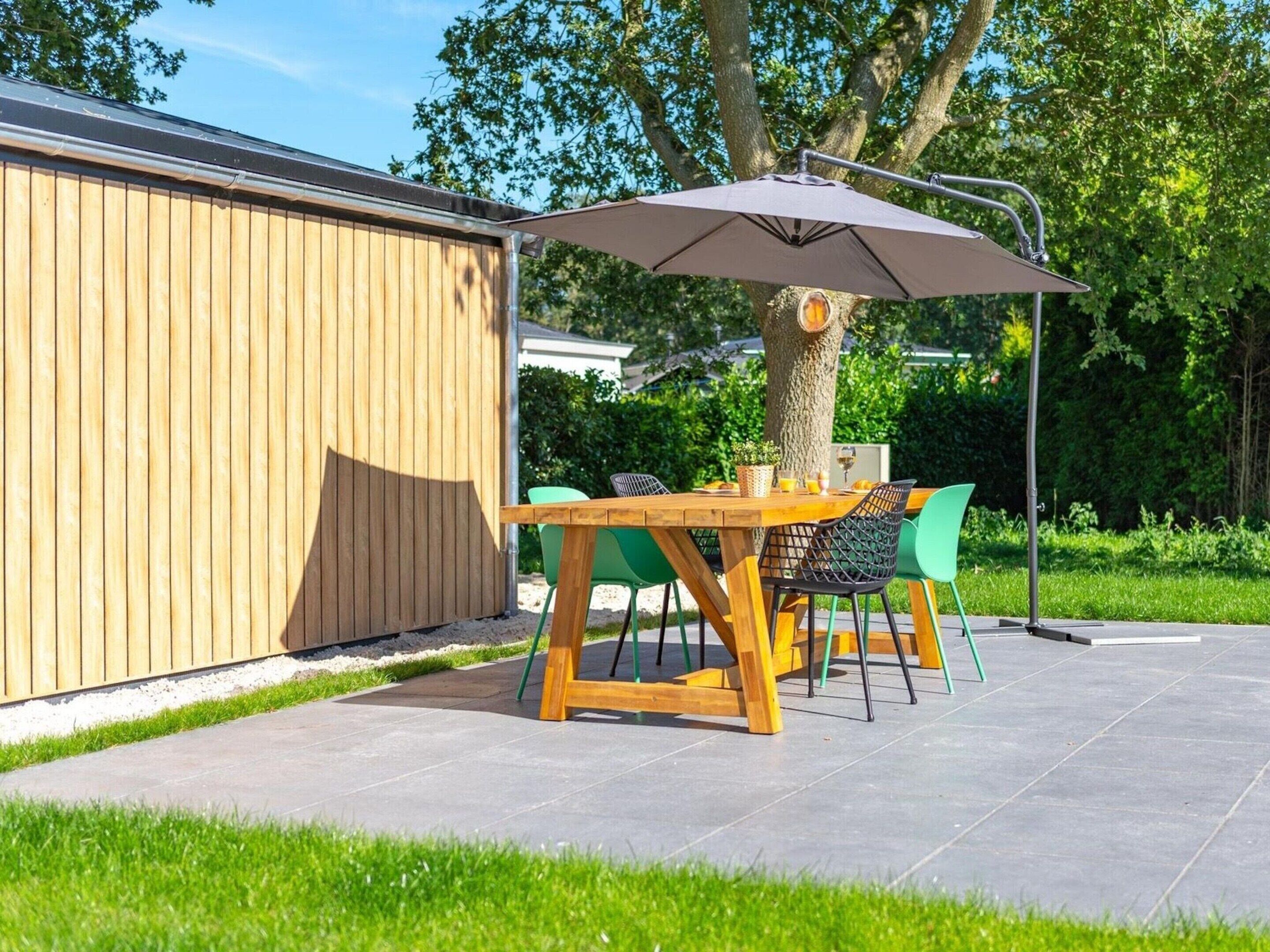 An outdoor patio with a wooden table and chairs, a large umbrella, and a tree.