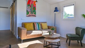 A modern living room with a sofa, a chair, a coffee table, and a colorful wall hanging. - Cozy Chalet With Unobstructed Views (Hoogersmilde)