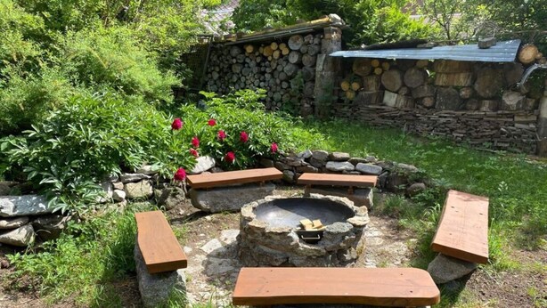A rustic outdoor seating area with stone benches and a fire pit surrounded by greenery and a stone wall. - Yellow House Modern Retreat (Cesky Jiretin)