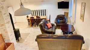 A modern living room with a sofa, a leather chair, a dining table, and a TV. - Yellow House Modern Retreat (Cesky Jiretin)