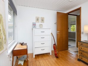 A room with a white dresser, a guitar leaning against the wall, and a wooden bench.