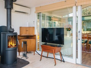 Una sala moderna con una estufa de leña, un televisor sobre un mueble de madera y un ventanal corredizo que da a un espacio exterior.