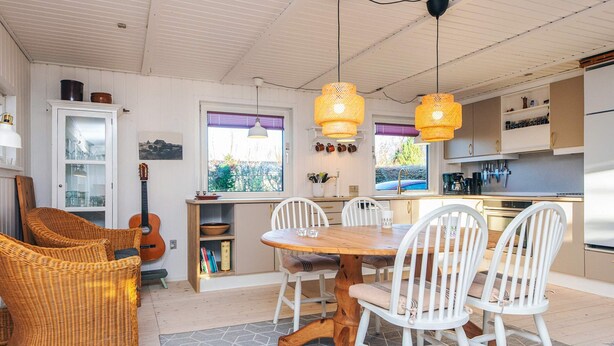 A modern kitchen with white cabinets, a dining table with white chairs, and a hanging light fixture.