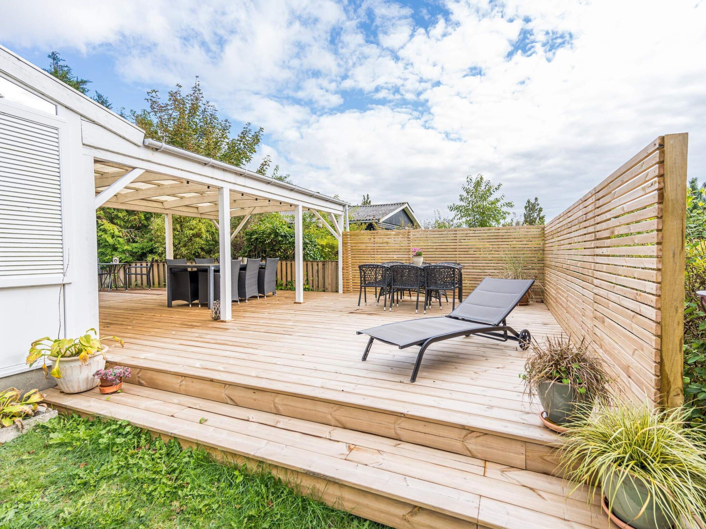 A covered outdoor patio with a table and chairs, a lounge chair, and potted plants.