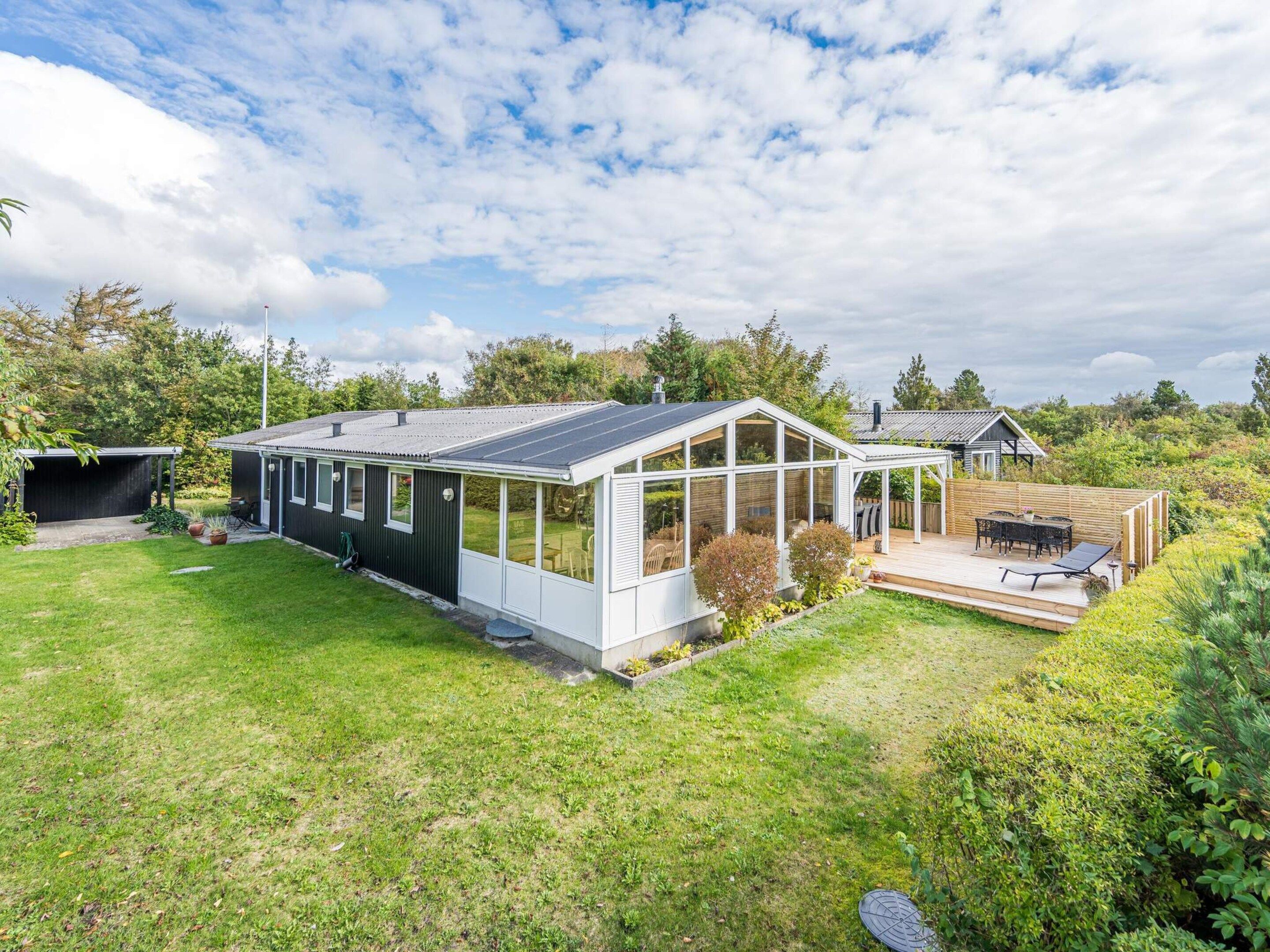 A modern house with a large glass conservatory, a covered patio, and a well-maintained garden.