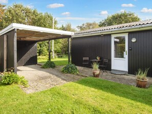 A covered outdoor area with a table and chairs, a door, and a small garden.