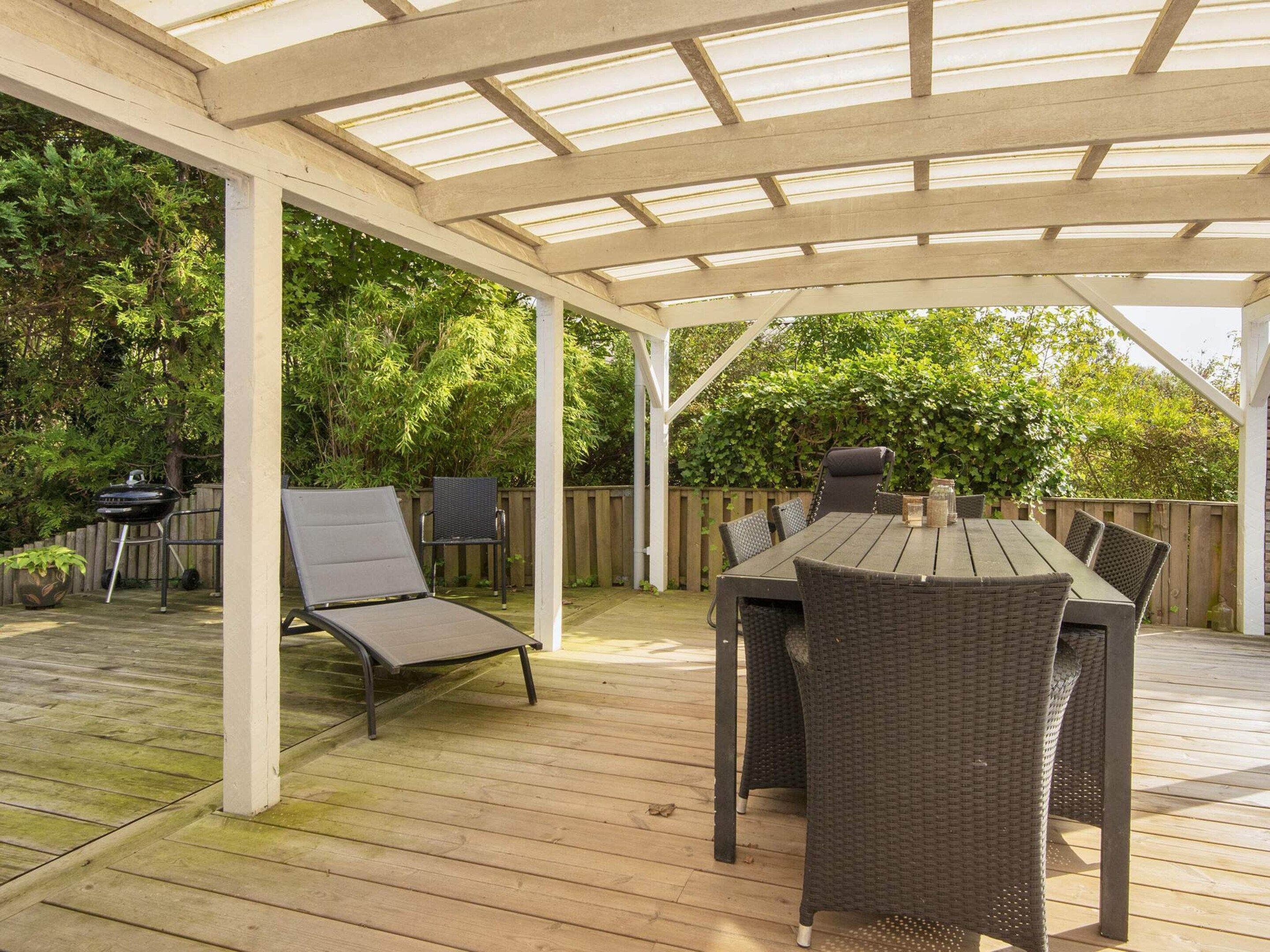 A covered patio with a table and chairs, a grill, and a lounge chair.