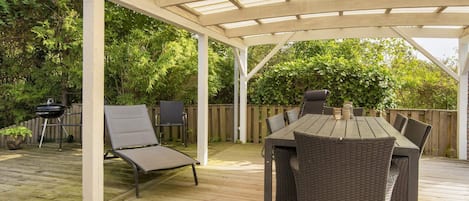 A covered patio with a table and chairs, a grill, and a lounge chair.