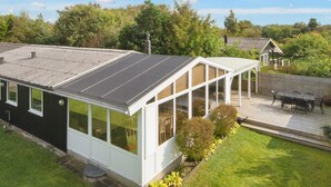A modern house with a large glass conservatory, a deck, and a well-maintained garden.