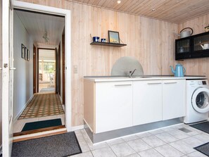 A compact kitchen with a washing machine, a shelf with decorative items, and a door leading to a hallway.