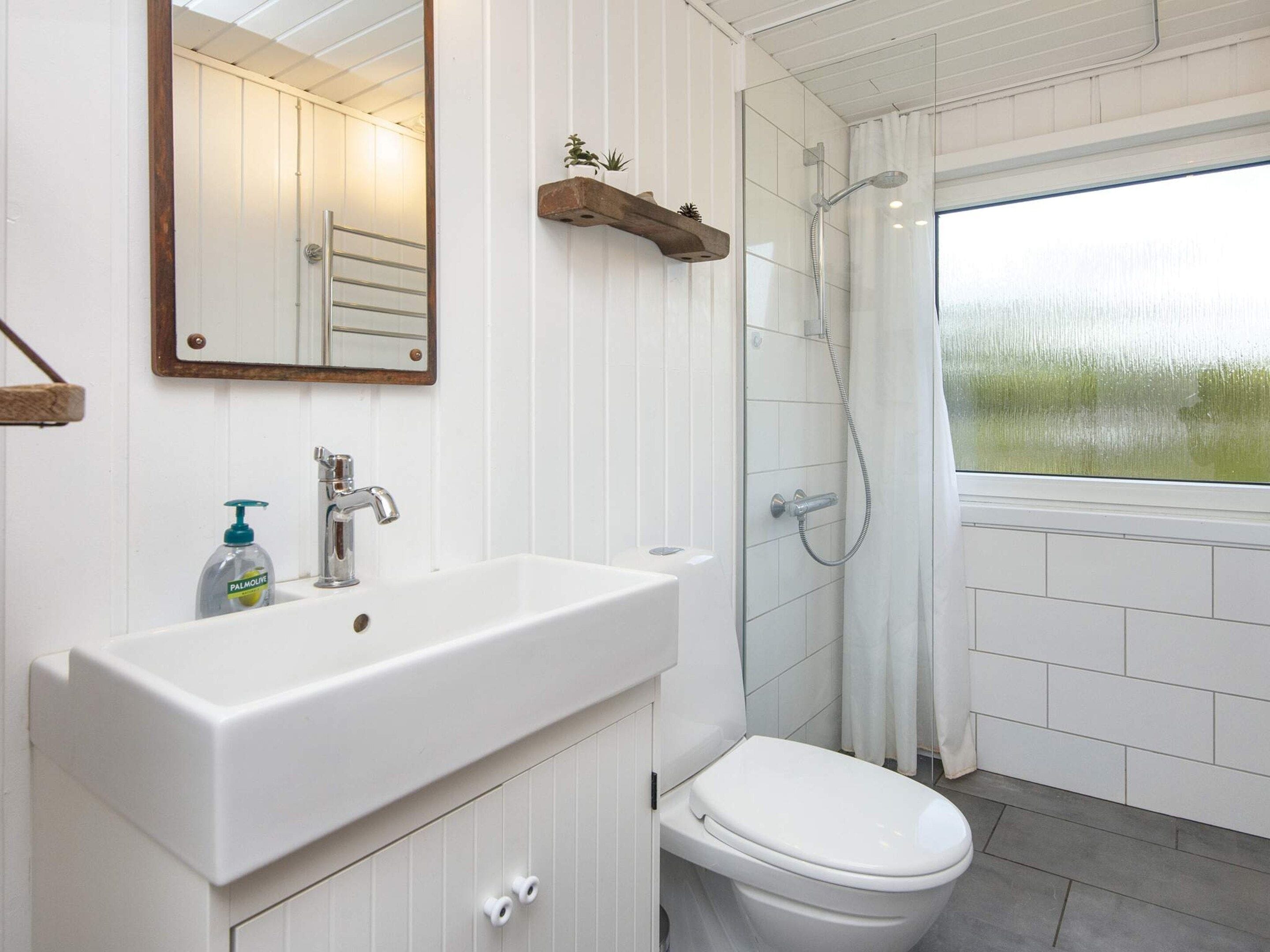 A bathroom with a white sink, a toilet, a shower, and a window with a view of greenery.