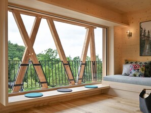 A room with a large window, wooden beams, a bed with colorful pillows, and a wall-mounted lamp. - Oma Ludwin 2 Comfortable Holiday Residence (Sasbachwalden)
