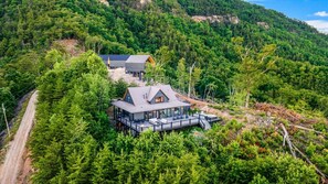 A modern house with a deck, surrounded by dense forest.