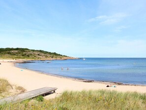 Ein Strand mit einer Holzsteg, ruhigem Wasser und einem Segelboot in der Ferne.