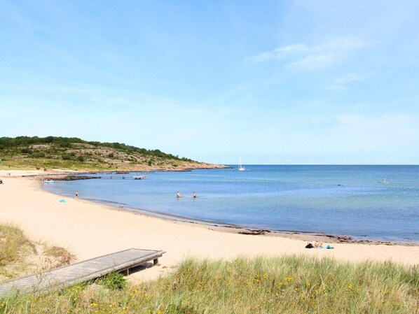 A beach with a wooden pier, calm water, and a sailboat in the distance. - 6 Person Holiday Home in Allinge (Allinge)