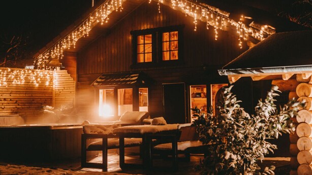 Una cabaña de madera con porche cubierto, luces colgantes y una sauna.
