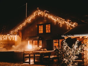 Una cabaña de madera con porche cubierto, luces colgantes y una sauna.