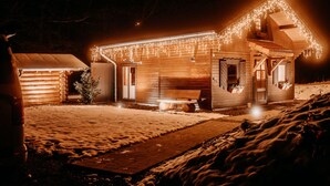 Una cabaña de madera con nieve en el suelo, un banco de madera y luces colgantes.