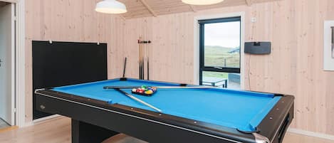 A pool table with balls and cues, a window with a view, and wooden walls.