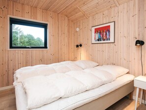 A room with wooden panel walls, a bed with white bedding, a window with a view of trees, and a framed picture on the wall. - 5 Star Holiday Home in Fano (Fano)