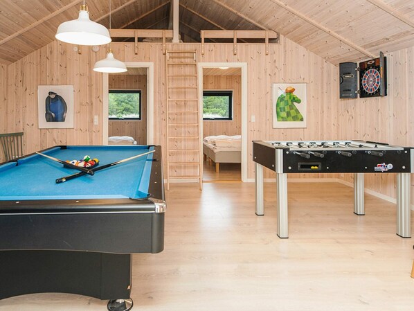 Une pièce équipée d’une table de billard, d’un baby-foot et d’un jeu de fléchettes. Une échelle donne accès à une zone de couchage située en hauteur.