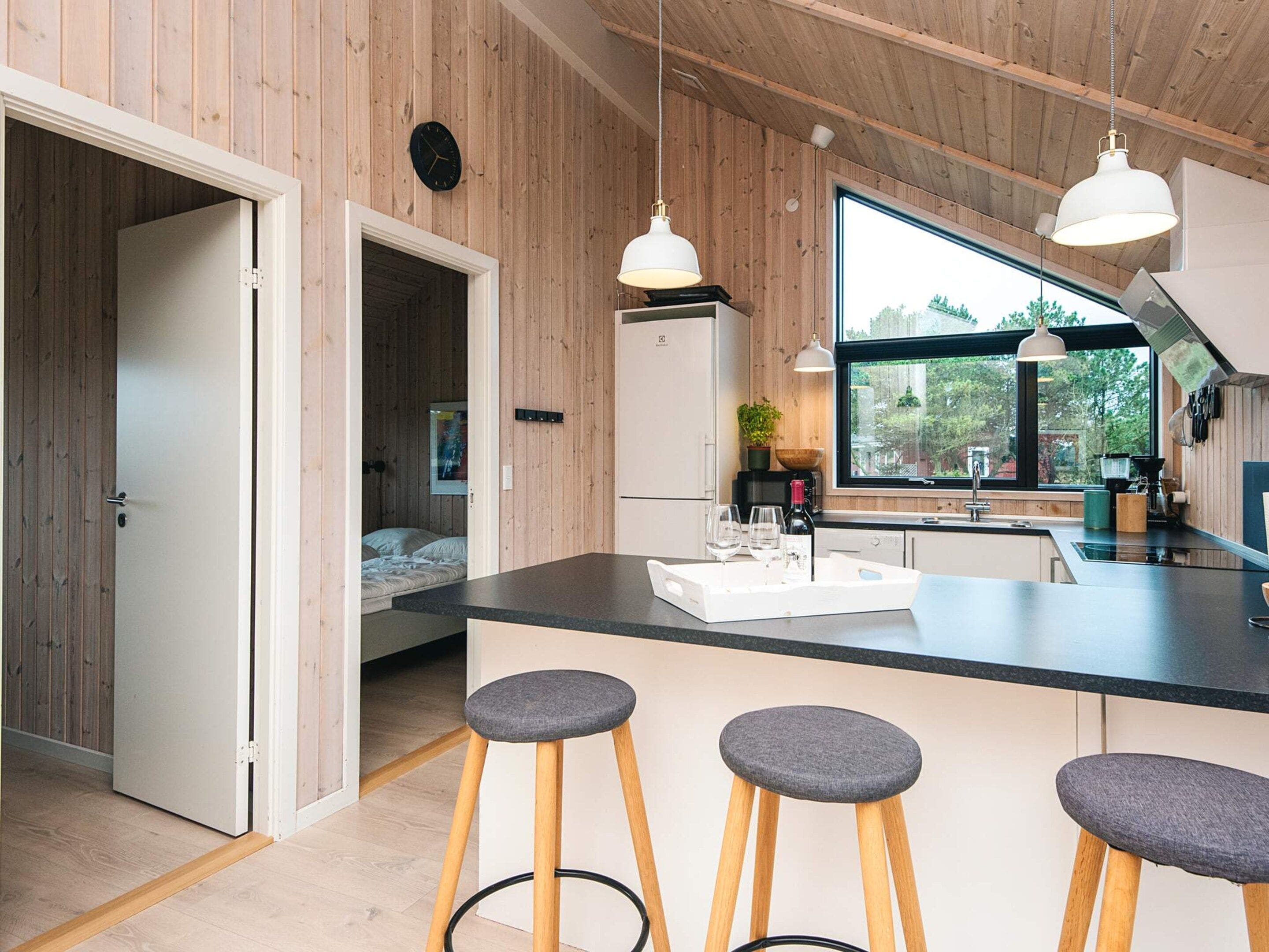 A modern kitchen with wooden walls, a large window, and a bar area with stools.