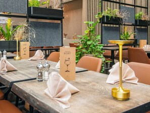 Un ambiente de restaurante con mesas y sillas de madera, y plantas en macetas.
