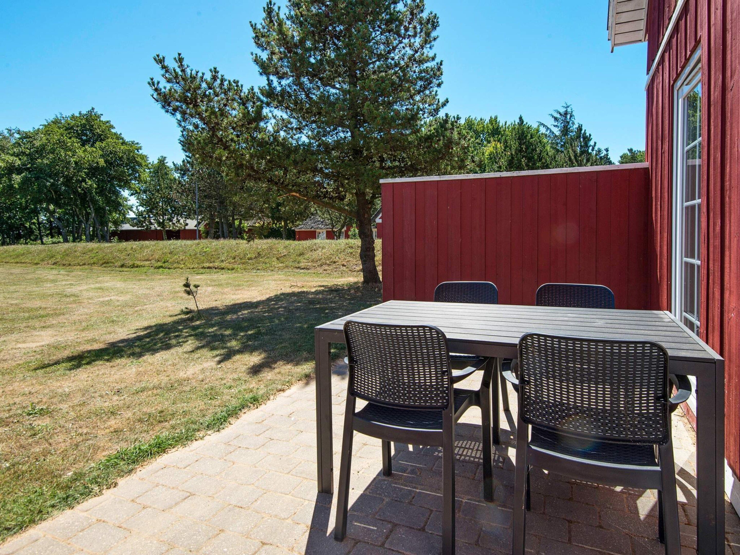 A patio with a table and chairs, a red building, and a grassy area with trees.