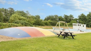Une aire de jeux avec un toboggan coloré, des balançoires et une table de pique-nique.