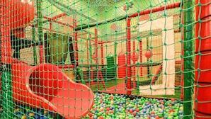 Un espace de jeux avec un toboggan rouge et une piscine à balles remplie de balles multicolores.
