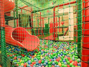 Un área de juegos con un tobogán rojo y un foso de pelotas lleno de bolas multicolores.