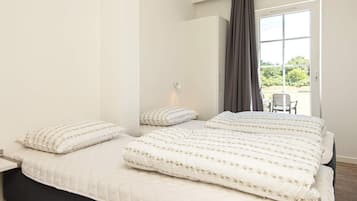 Ein Schlafzimmer mit einem großen Bett, einem Nachttisch und Blick ins Freie durch ein Fenster mit Vorhängen.