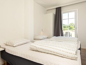 A bedroom with a large bed, a bedside table, and a view of the outdoors through a window with curtains. - 6 Person Holiday Park Home in Blavand (Blavand)
