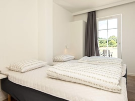 Un dormitorio con una cama grande, una mesita de noche y vistas al exterior a través de una ventana con cortinas.