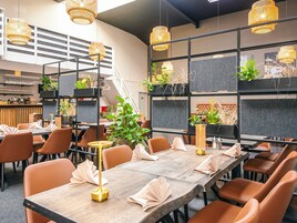 A modern restaurant with long tables, orange chairs, and hanging wicker lamps.